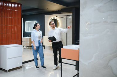 Satış danışmanı banyo tasarımı seçeneklerini dekoratif aydınlatma ve modern donanımlı çağdaş sergi salonunda bulunan potansiyel alıcıya açıklıyor.