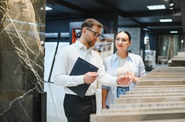 Satıcının elinde pano var. Seramik fayans örneklerini döşeme ve tesisat dükkanındaki müşteriye sunuyor.