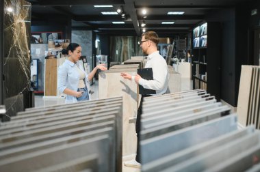Hırdavatçı dükkanında çeşitli seramik numuneler sunan mağaza asistanı, ev geliştirme projeleri seçeneklerini tartışıyor