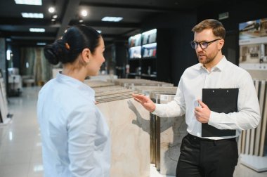 Satış elemanı seramik fayans seçeneklerini seçmede müşteriye yardımcı olurken perakende satış mağazasında çeşitli renkler, dokular ve desenleri tartışır.
