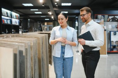 Gülümseyen bayan müşteri dairesi için seramik fayanslar seçiyor, hırdavatçıdan profesyonel tavsiyeler alıyor.