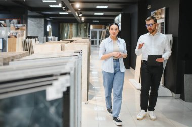 Tesisat ve fayans dükkanında müşteriye farklı seramik fayanslar gösteren bir tezgahtar.