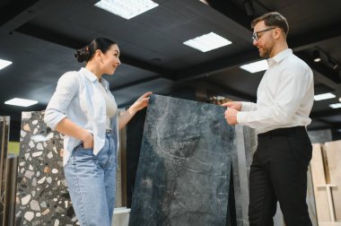 Mağazadaki bir müşteriye seramik fayans örneği sunan mağaza asistanı, ev geliştirme için seçim ve tasarım seçeneklerinde yardımcı oluyor