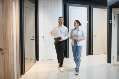 Bir hırdavatçıda çeşitli iç kapılar sergilenirken, gülümseyen bir mağaza asistanı bir kadın müşteriyle meşgul oluyor.