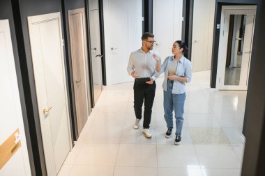 Kadın müşteri ve erkek satıcı çeşitli kapı vitrinleriyle çevrili seramik fayans ve tesisat mağazasında seçenekleri tartışıyor.