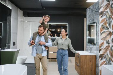 Mutlu bir aile, bir tesisat dükkanında yeni banyo demirbaşlarını seçiyor, farklı seçenekleri tartışıyor ve işaret ediyor.