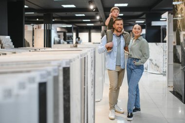 İyi aydınlatılmış bir tesisat dükkanında seramik seçenekler arayan mutlu çift, çeşitli malzemeler ve ev yenileme tasarımları sergiliyorlar.