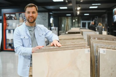 Gülümseyen mimar modern bir fayans dükkanında banyo veya mutfak tadilatı için seramik fayanslar seçiyor.