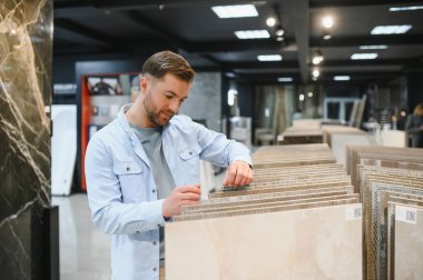 Modern bir mağazada çeşitli tasarım seçenekleriyle çevrili seramik fayanslar arıyoruz. Mükemmel fayansları seçmeye odaklanmış görünüyorlar.