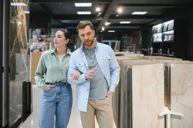 Bir hırdavatçıda yürüyen ve seramik fayansları seçen çift farklı örnekleri tartışıyor ve işaret ediyor.