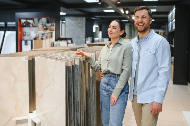 Gülümseyen bir çift modern bir mağazada seramik fayanslara bakıyor, ev yenileme ve iç tasarım seçimlerine ilgi gösteriyor