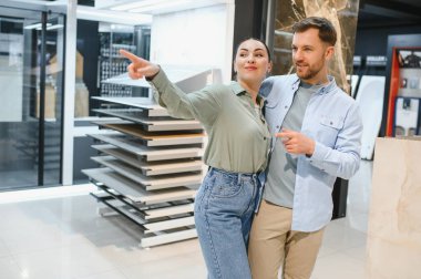 Bir hırdavatçıdaki seramik fayans örneklerini gösteren çift, ev yenileme ve iç tasarım hakkında konuşuyor