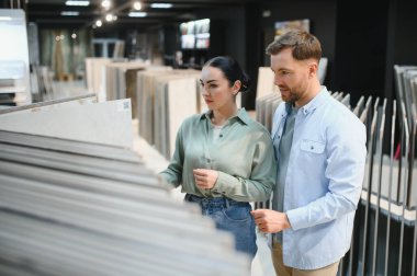 Modern bir hırdavatçıda seramik seramik fayanslar keşfeden genç bir çift, heyecanla seçenekleri ve stilleri tartışıyor.