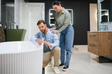 Banyodaki mobilya dükkanında beyaz bir küveti inceleyen çift, evlerini yenilemeyi planlıyor.