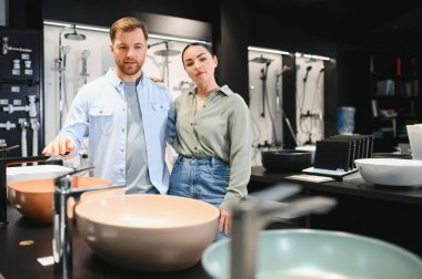 Tesisatçı dükkanında seramik lavabo seçen çift banyo yenileme için mobilya seçiyor.