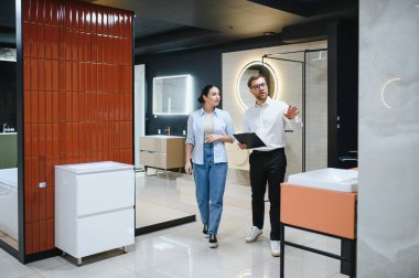 Profesyonel tezgahtar, tesisat mağazasında kadınlara banyo mobilyalarını gösteriyor, seramik fayanslar ve diğer ürünleri seçmesine yardım ediyor.