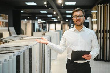 İyi ışıklandırılmış seramik ve su tesisatı mağazasında bilgili bir satıcıyla görüşen kadın alıcı çeşitli fayans seçeneklerini sergiliyor.
