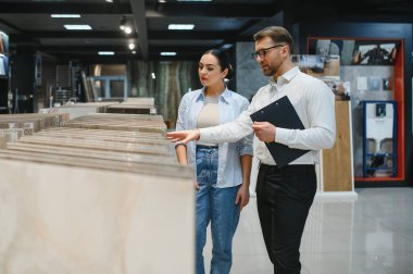 Modern bir hırdavatçıda kadın müşteriye farklı seramik örnekler gösteren tezgahtar doğru seçimi yapmasına yardımcı oluyor.