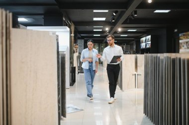 Profesyonel satıcı, bir kadın müşteriye seramik ve su tesisatı dükkanında yürürken ve tartışırken farklı seramik fayanslar gösteriyor.