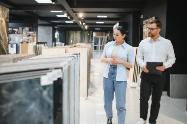 Modern bir sıhhi tesisat ve fayans dükkanında dairesi için seramik fayanslar seçen bir kadın müşteri.