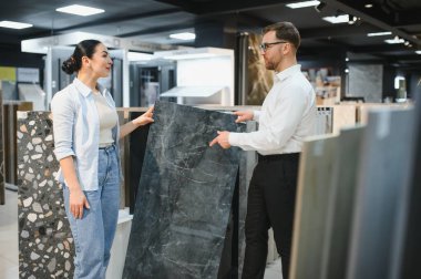 Seramik ve sıhhi tesisat dükkanında kadın müşteriye farklı seramik fayans modelleri gösteren bir satıcı.