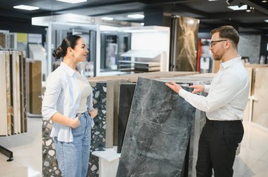 Satış elemanı seramik fayans sunan bir kadın müşteriye fayans ve tesisat mağazasında ev geliştirme ve tasarım seçeneklerini tartışıyor.