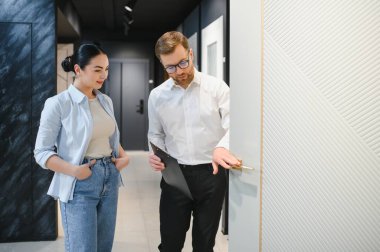 Profesyonel mağaza asistanı, bir tesisat ve seramik dükkanında modern beyaz kapıyı bayan müşteriye gösteriyor.