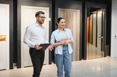 Profesyonel satıcı elinde pano ile mobilya mağazasında kadın müşterilere farklı kapı modelleri gösteriyor. Satın alma seçeneklerini tartışıyor.