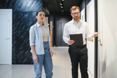 Satıcının elinde pano var. Seramik fayans ve tesisat dükkanındaki kadın müşterilere iç kapıları gösteriyor.