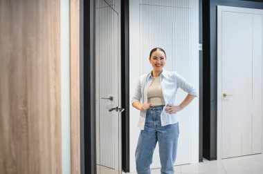 Seramik fayans ve su tesisatı mağazasında gülümseyen ve poz veren kendine güvenen satıcı kadın, çeşitli modern kapı modelleri sergiliyor.