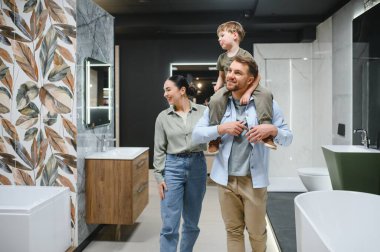 Mutlu bir aile seramik fayans ve su tesisatı dükkanında banyo demirbaşlarını seçiyor, baba oğlunu omuzlarında taşıyor.