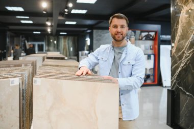 Ev geliştirme mağazasından seramik fayanslar seçen, örneklere dokunan ve yenileme projesi için kararlar alan bir adam.