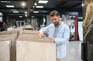 Bir mağazadan seramik fayanslar seçen, örneklere dokunan ve ev yenileme veya iç tasarım projesi için seçimini yapan bir adam.