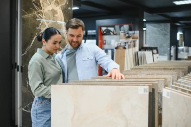 Genç bir çift, bir hırdavatçıda seramik fayanslar seçiyor. Ev yenileme projelerini planlıyorlar.