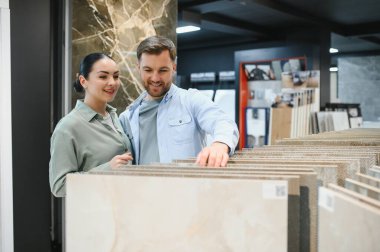 Gülümseyen bir çift bir hırdavatçıda seramik fayanslar seçiyor, banyo yenileme projelerini planlıyorlar.