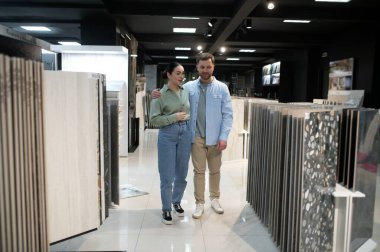 Tesisatçı dükkanında seramik fayanslar geziyor, ev tadilatı seçeneklerini değerlendiriyor, çeşitli fayans tasarımları ve bitirmeler ile çevrili.