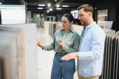 Genç çift daireleri için seramik fayanslar seçerken bir hırdavatçıda seçenekleri gözden geçiriyorlar, stilleri ve kaliteyi tartışıyorlar.