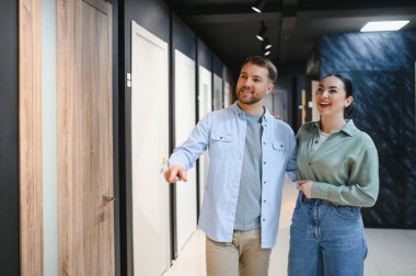 Mutlu çift ahşap kapıyı işaret ediyor, yeni bir apartman dairesi için mobilya seçiyor ve satın alıyor.