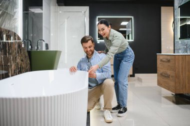 Çift, modern banyo tasarımı ve yenileme fikirlerine ilgi gösteren seramik fayans ve tesisat mağazasında zarif bir küveti inceliyor.