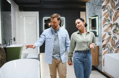 Mutlu çift yeni şık bir banyo küveti seçerken el ele tutuşuyor ve canlı bir banyo eşyalar mağazasında batıyor, alışveriş deneyiminin tadını çıkarıyorlar.