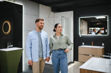 Banyo eşyaları galerisinde el ele yürüyen seramik fayansları, lavaboları ve duş kabinlerini seçen çift.