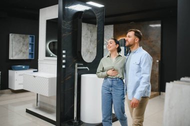 Genç çift banyo eşyaları mağazasında yürüyor, seramik fayansları, lavaboları ve mobilyaları seçiyorlar.