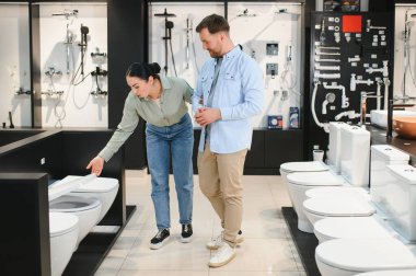 Asistan, tuvaletteki mobilya dükkanındaki bir çifte farklı klozetler gösteriyor. Doğru olanı seçmelerine yardım ediyor.