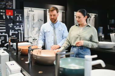 Tesisatçı dükkanında seramik lavabo seçen çift, banyo yenileme projesi için alışveriş yaparken tartışmalara giriyorlar.