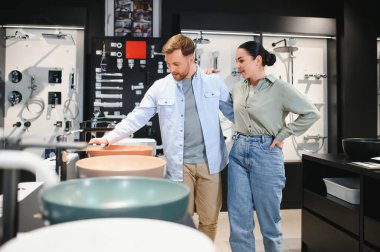 Çeşitli stil ve seçenekleri göz önünde bulundurarak, özel bir mağazadan banyo malzemeleri alırken seramik lavaboları seçen çift.