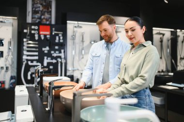 Çift modern bir seramik fayans ve tesisat dükkanında modern banyo tasarım seçeneklerinin sergilendiği şık lavaboları ve muslukları inceliyor.