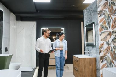 Satıcı, modern seramik fayans ve su tesisatı mağazasındaki müşterilere banyo demirbaşlarını gösteriyor.