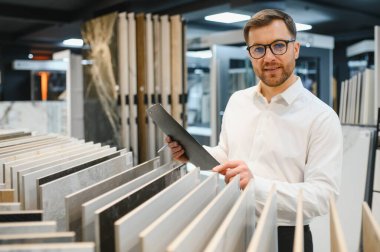 Modern bir tesisat ve fayans dükkanında müşteriye farklı seramik fayanslar gösteren bir satıcı.