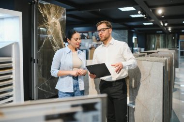Profesyonel mağaza asistanı bir kadın müşteriye farklı seramik örnekler gösteriyor. Projesi için doğru malzemeyi seçmesine yardım ediyor.