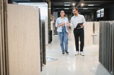 Modern bir tesisat ve fayans dükkanında müşteriye farklı seramik fayanslar gösteren bir satıcı.